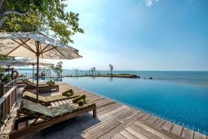 ein Pool mit Stühlen und Sonnenschirmen neben dem Meer in der Unterkunft Green Bay Phu Quoc Resort & Spa in Phu Quoc