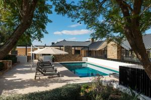 a swimming pool with chairs and an umbrella next to a house at Kingsford The Barossa in Concordia