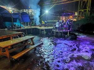 a group of people sitting in a purple pond at night at Camping Pines singkur reverside in Bandung