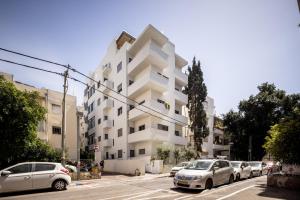 a white building with cars parked in a parking lot at Heart of Tel Aviv Garden Oasis by Sea N' Rent in Tel Aviv