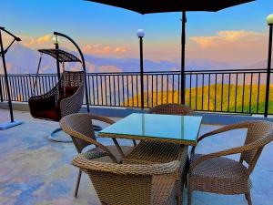 una mesa con sillas y una sombrilla en el balcón en The Pine Woods - A Four Star Luxury Resort in Mussoorie, en Mussoorie
