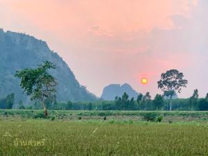 un tramonto su un campo con un albero e montagne di บ้านส่าหรีโฮมสเตย์ a Lan Sak