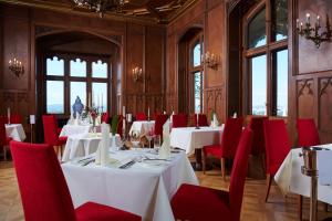 un comedor con mesas blancas y sillas rojas en Hotel Schloss Eckberg en Dresden