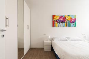 ミラノにあるBilocale con balcone vicino palazzo del ghiaccioの白いベッドルーム(ベッド1台付)が備わります。壁には絵画が飾られています。