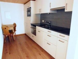 cocina con armarios blancos, fregadero y suelo de madera en Hotel Rhätia, en Luzein