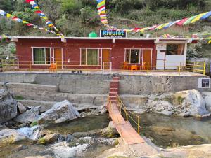 a building with a bridge in front of a river at Rivulet Resort & Camping in Mussoorie