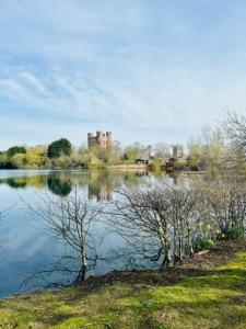 a lake with trees and a castle in the background at Bull Rush Retreats luxury hot tub lodge at Tattershall Lakes in Tattershall