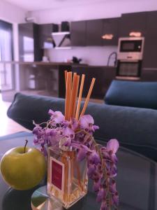 een vaas met paarse bloemen en een appel op een tafel bij AURORA suites in Ghiroda