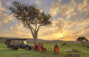 een groep mensen die aan tafels onder een boom zitten bij sunshine maasai Mara safari camp in Kenya in Sekenani
