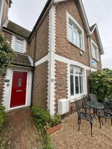 Casa de ladrillo con puerta roja, mesa y sillas en Downs Gate Cottage, en Eastbourne