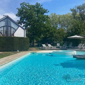 uma grande piscina azul com cadeiras e um guarda-sol em Gîte 7 personnes- Le Refuge du Saule em Burdinne