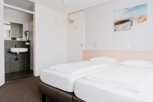1 dormitorio con 2 camas blancas y baño en Hotel Kodde, en Aagtekerke