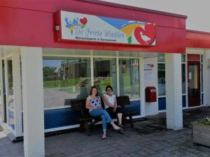 two women sitting on a bench outside of a store at Chalet with garden near Wadden Sea in Tzummarum
