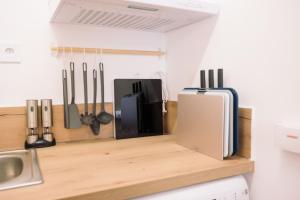 a kitchen counter with utensils and a refrigerator on a shelf at L’Albizia- Centre -TV WIFI-Cozy in Narbonne +7 photos