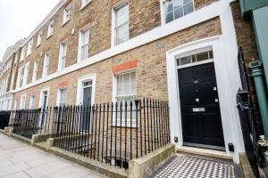 a brick building with a black door and a fence at Spacious, Bright & Cosy ~ Ideal Victoria Location! in London