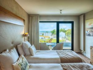 a hotel room with a bed and a large window at Côte Ouest Hôtel Thalasso & Spa Les Sables d'Olonne - MGallery in Les Sables-dʼOlonne