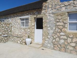a stone house with a white door and a plant at Mariette's Cottage in Arniston +4 photos