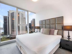 sypialnia z dużym białym łóżkiem i dużymi oknami w obiekcie The Sebel Residences Melbourne Docklands Serviced Apartments w Melbourne