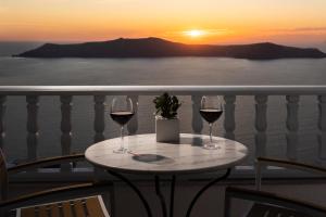a table with two glasses of wine on a balcony with the sunset at Nevma Suites in Firostefani