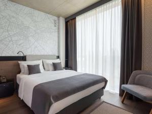 a bedroom with a bed and a chair and a window at Mövenpick Zagreb in Zagreb