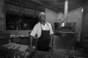 Um homem de avental em pé numa cozinha. em Les Lauriers Eco Hotel em Anse Volbert Village