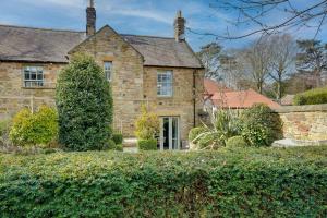 an old stone house with a hedge in front of it at Spence Lodge: Beautiful 2-Bedroom Stone Cottage in Alnmouth