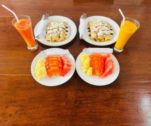 four plates of food on a wooden table with three drinks at Bupon House Jepun Room in Gianyar