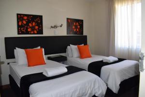 Habitación con 2 camas y almohadas de color naranja y blanco. en Premiere Classe Apartment Hotel en Johannesburgo