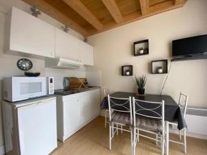 eine Küche mit einem Tisch, Stühlen und einer Mikrowelle in der Unterkunft Appartement au Parc de la Grange in Jard-sur-Mer