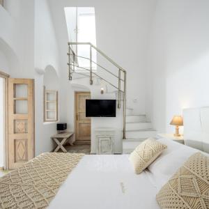 a white bedroom with a bed and a tv at MyBoZer Hotel Kallisto in Imerovigli