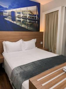 a bedroom with a white bed with a painting on the wall at Apartamento em Brasília, Àguas Claras, S4 Hotel in Brasilia