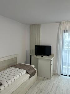 a white bedroom with a bed and a television at Pensiunea La Cazemata Bucov in Satu Bucovei