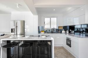 a white kitchen with a large island with bar stools at Yulunga - Direct Beachfront in Narrabeen