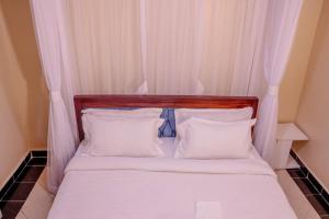 uma cama com cabeceira em madeira e almofadas brancas em Dayo Suites & Hotel em Nairobi