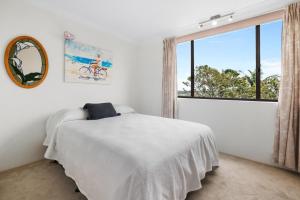 a white bedroom with a bed and a large window at Tarquin - Harbour Views in Sydney