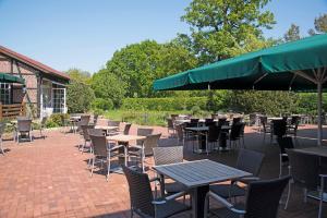 eine Terrasse mit Tischen und Stühlen und einem grünen Sonnenschirm in der Unterkunft Landhaus Bruckmann in Saerbeck