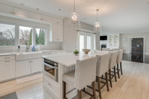a white kitchen with a large island with bar chairs at Spacious Inverness Home about 36 Mi to Chicago! in Barrington Hills