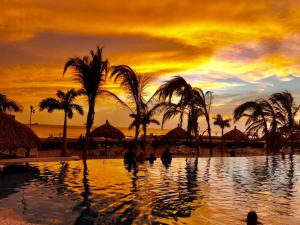 puesta de sol sobre una piscina en una playa con palmeras en Samaria Club de playa, Sector Pozos Colorados, en Santa Marta