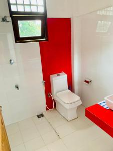 baño con aseo blanco y pared roja en Privet Home Stay, en Wattala