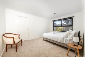 a bedroom with a bed and a chair and a window at Sensational New Townhouse in Canberra