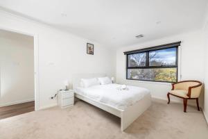a white bedroom with a bed and a chair at Gorgeous Hawker Townhouse in Canberra