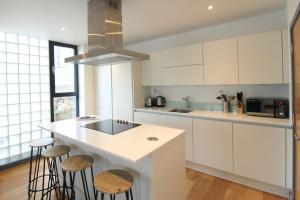 a kitchen with white cabinets and a island with stools at Canning Town by Viridian Apartments in London