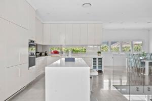 a white kitchen with white cabinets and a table at Rodd Point Luxury Haven: Waterfront Elegance with BBQ Terrace in Sydney