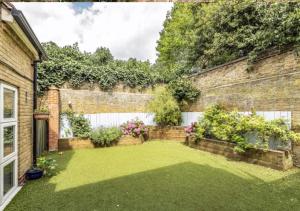 un patio trasero con una pared de ladrillo y césped verde en Welcome To Your Home en Londres