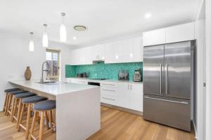 cocina con armarios blancos y nevera de acero inoxidable en Seaside Family Oasis - Anna Bay NSW, en Anna Bay