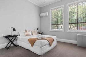 a white bedroom with a bed and two windows at Haven on Hunter - 500m to Civic Theatre in Newcastle