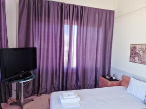 a bedroom with a bed with purple curtains and a tv at Kalogria Beach Apartments in Kalogria