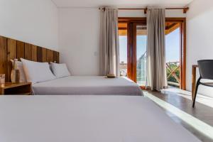 two beds in a hotel room with a window at Casa Nós de Vento - Praia do Prea in Cruz