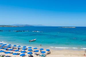a beach with blue umbrellas and people in the water at Boho City Hostel in Chania