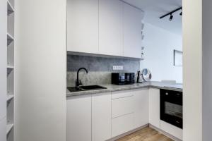 STAR stylish flat in a modern neighborhood في براتيسلافا: مطبخ أبيض مع دواليب بيضاء ومغسلة